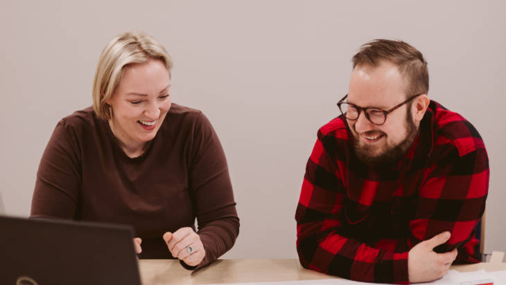 Kaksi opiskelijaa nauravat yhdessä tietokoneella ollessaan neuvotteluhuoneessa.